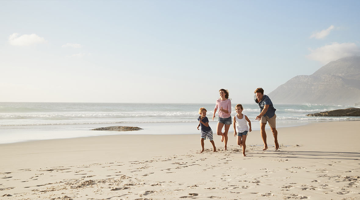family of four running across a sunny beach in the sun